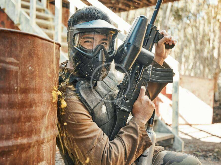 Person in tactical gear holding a rifle, smiling under a mask.