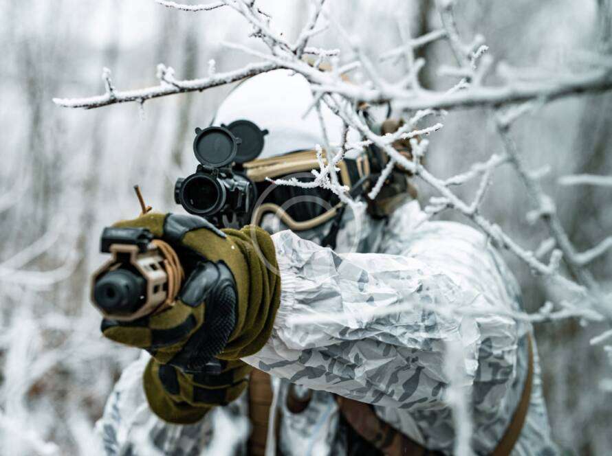 Sniper aiming through snowy branches in winter camouflage.